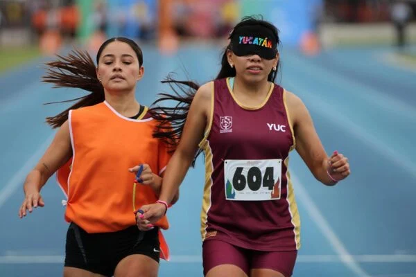 Atleta con uniforme de Yucatán corre junto a su guía en una pista de atletismo