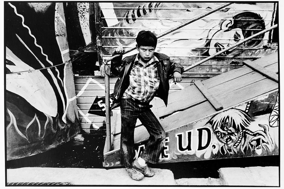Fotografía en blanco y negro de un niño junto a un juego mecánico de feria, obra de la colección del MUAC